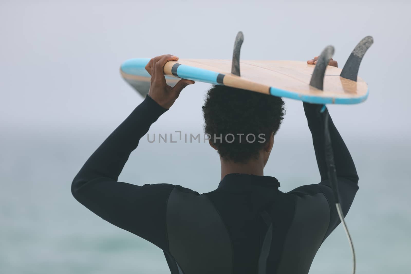 Rear view of young mixed-race male surfer carrying surfboard on her head at beach