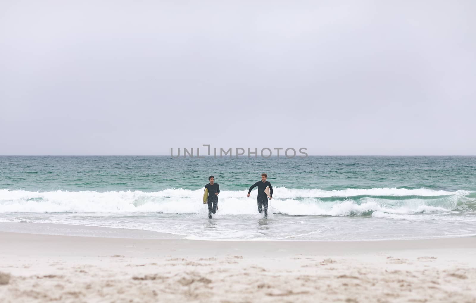 Front view of young multi-ethnic male friends running on beach while holding surfboards