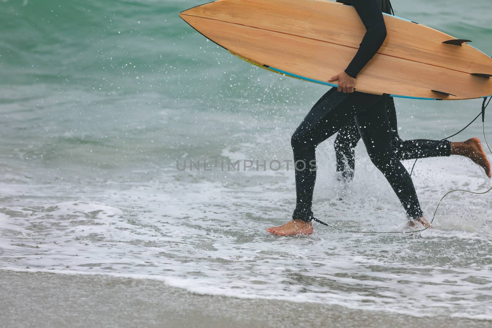 Low section of young multi-ethnic male friends walking on beach while holding surfboards