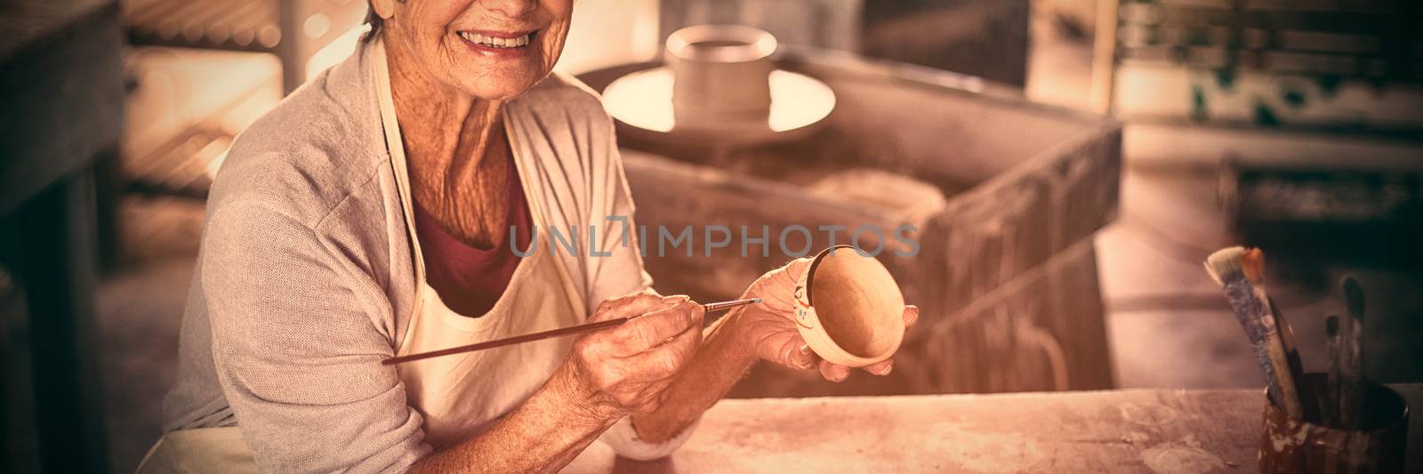 Portrait of female potter painting on bowl in pottery workshop