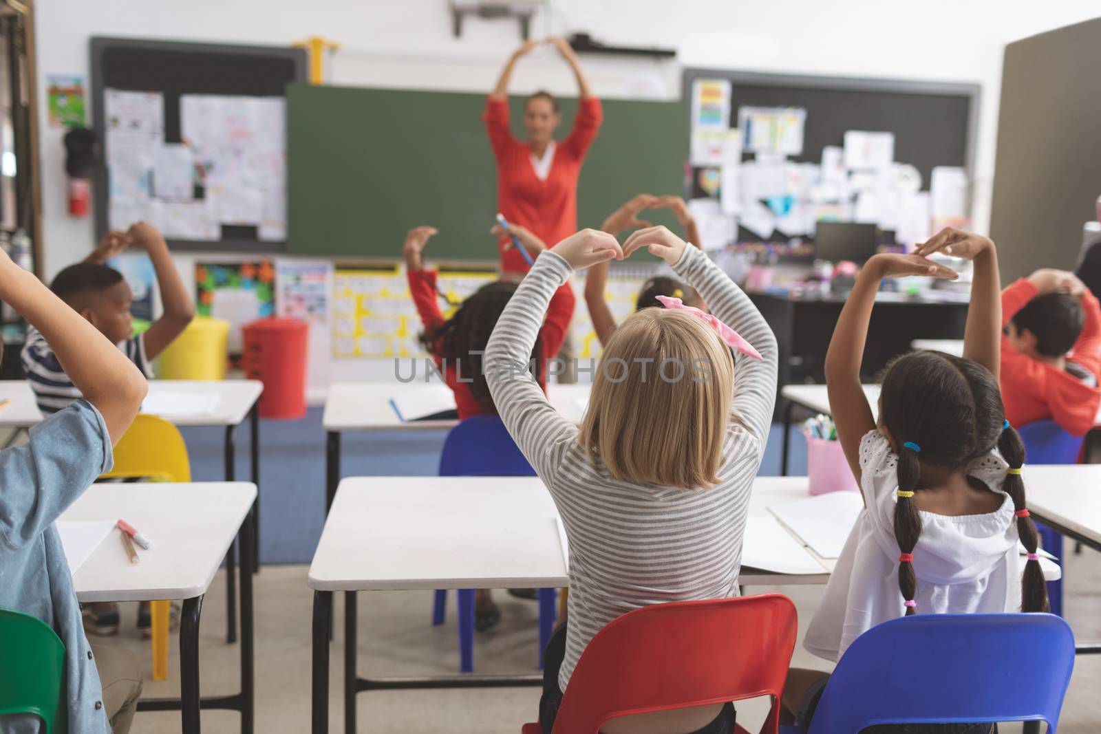 Rear view of mixte ethnicity school kids with arms up playing in the classroom at school