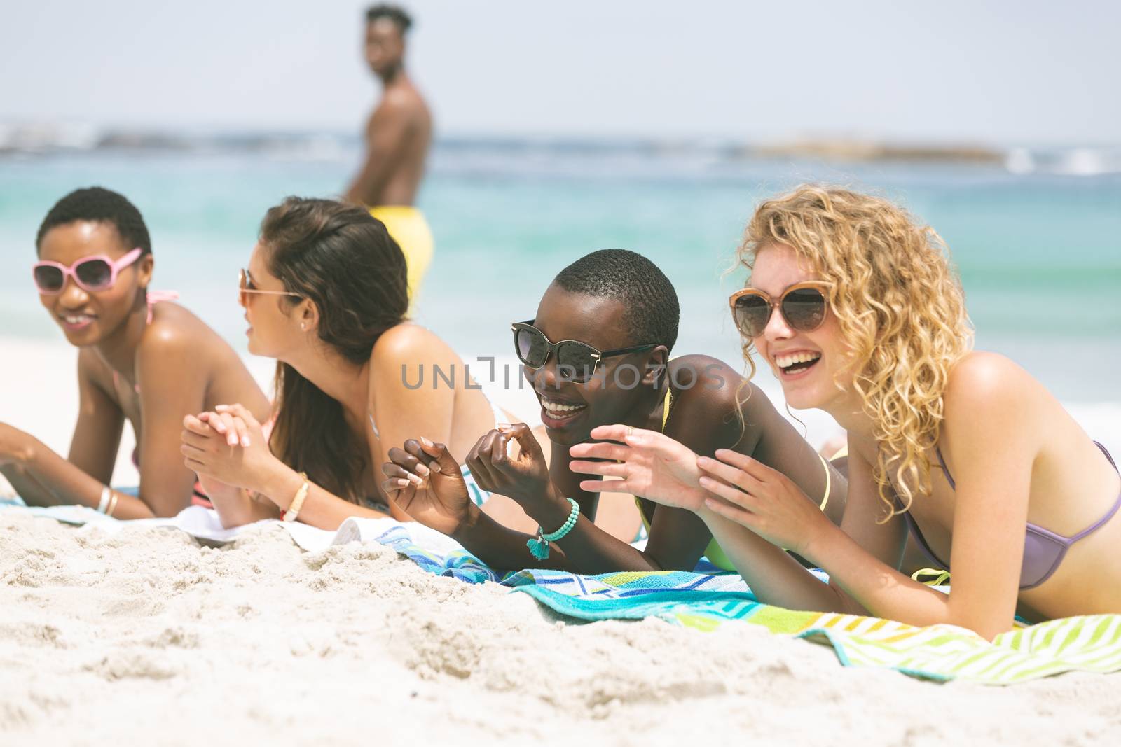 Front view of multi ethnic women interacting with each other while lying at beach on sunny day