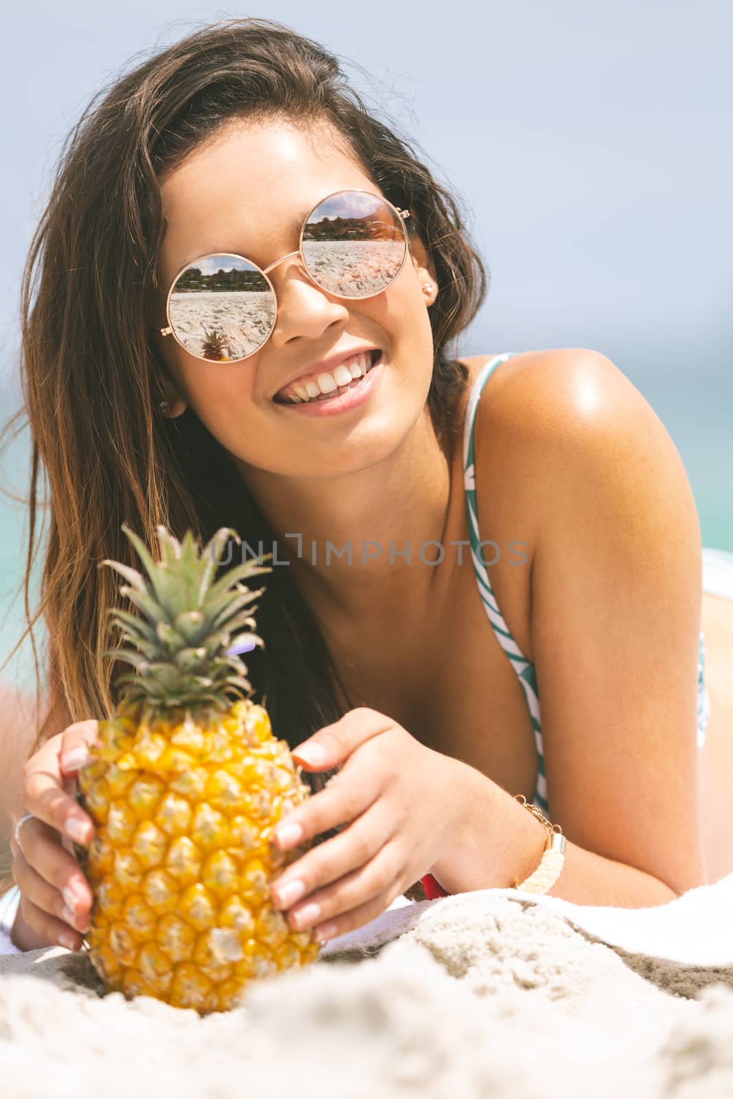 front view of caucasian woman lying at beach while having pineapple on sunny day