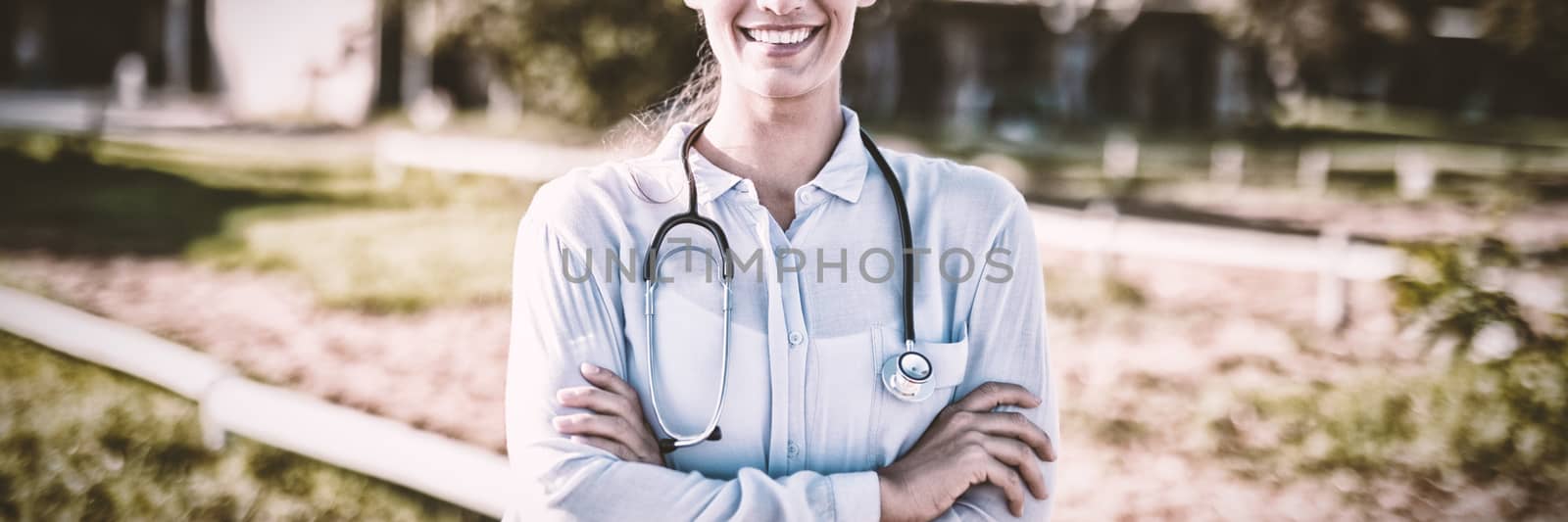 Smiling female vet with arms crossed standing at barn by Wavebreakmedia