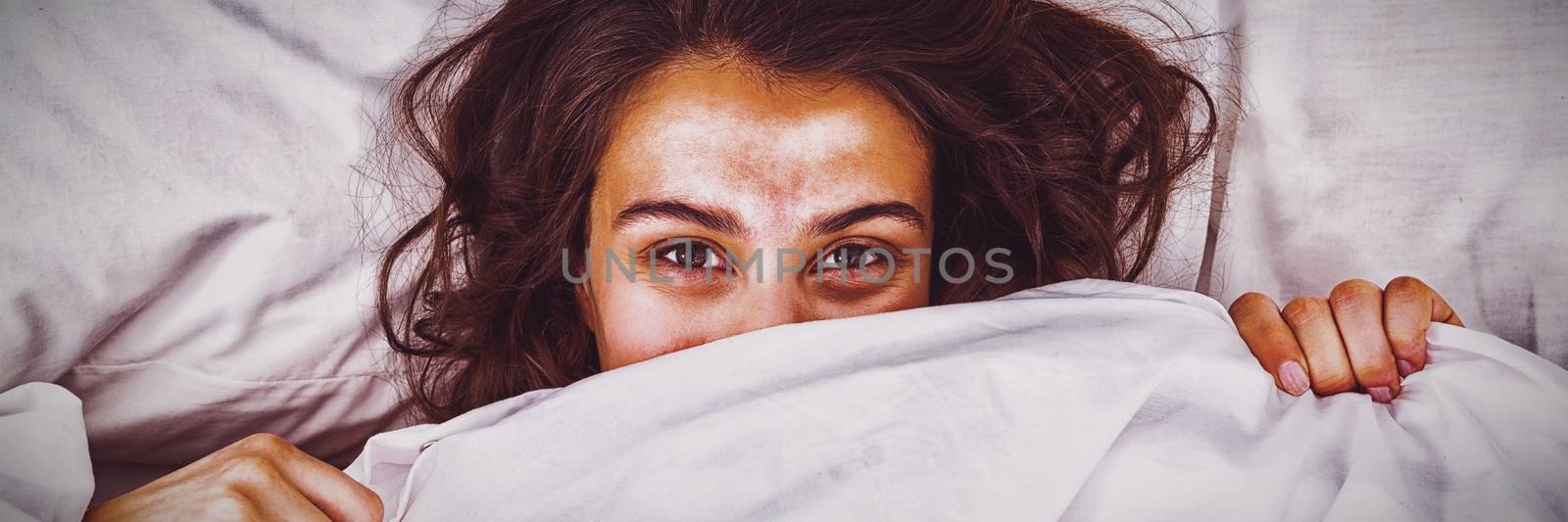 Woman hiding under blanket on bed by Wavebreakmedia