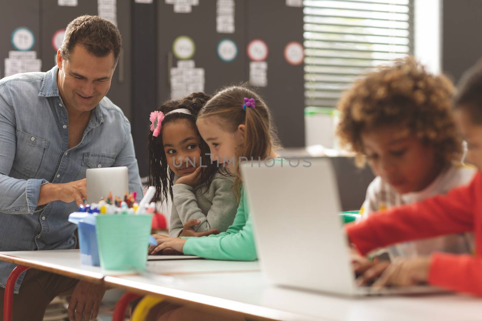 Side view of school kids using laptop in classroom while teacher discussing with students