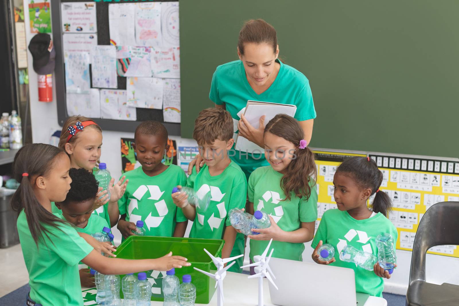 Front view of caucasian teacher and multi ethnic student discussing about green energy in classroom. Students holding plastic bottle