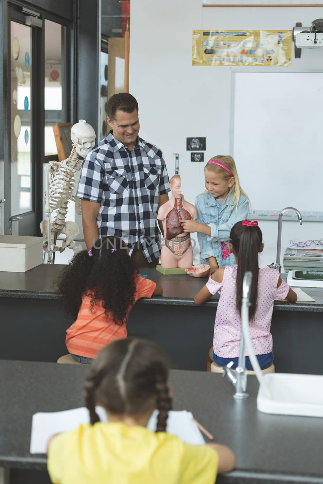 Front view of a Caucasian schoolgirl explaining to others school kids the human body with his teacher next to her