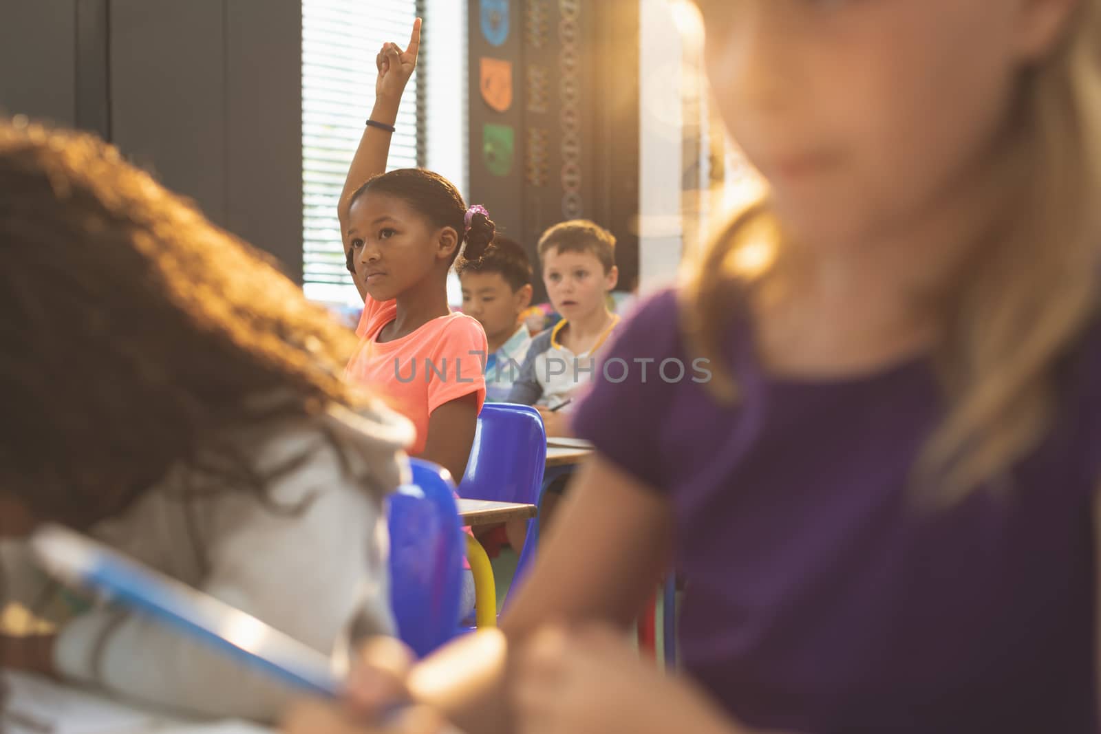 Front view of a schoolgirl raising hand while sitting in classroom at school