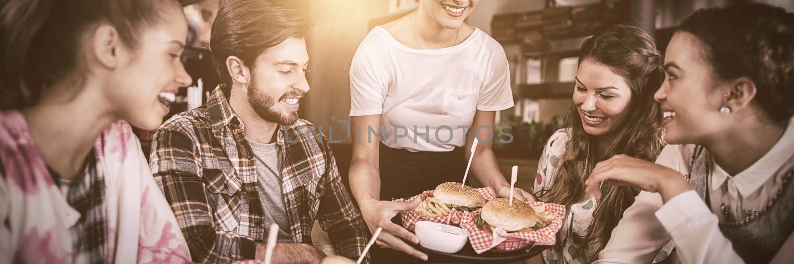 Young waitress serving burgers to customers in restaurant