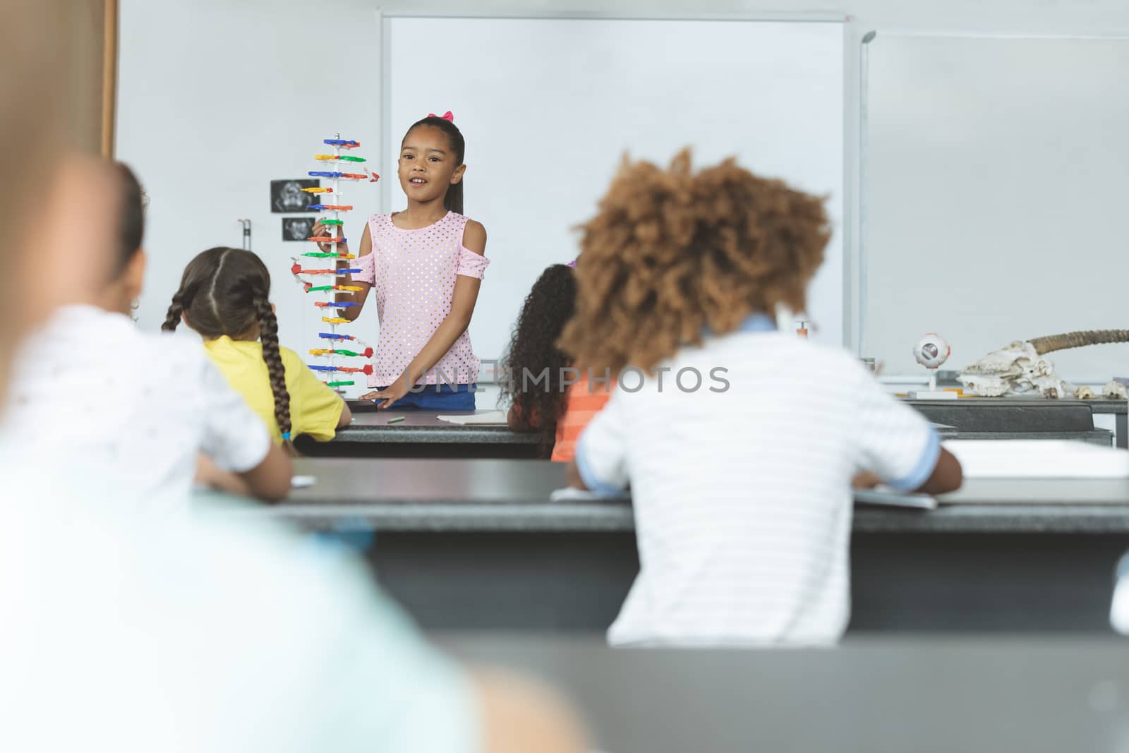 Front view of a schoolgirl interacting with his classmates over DNA structure model in classroom at school