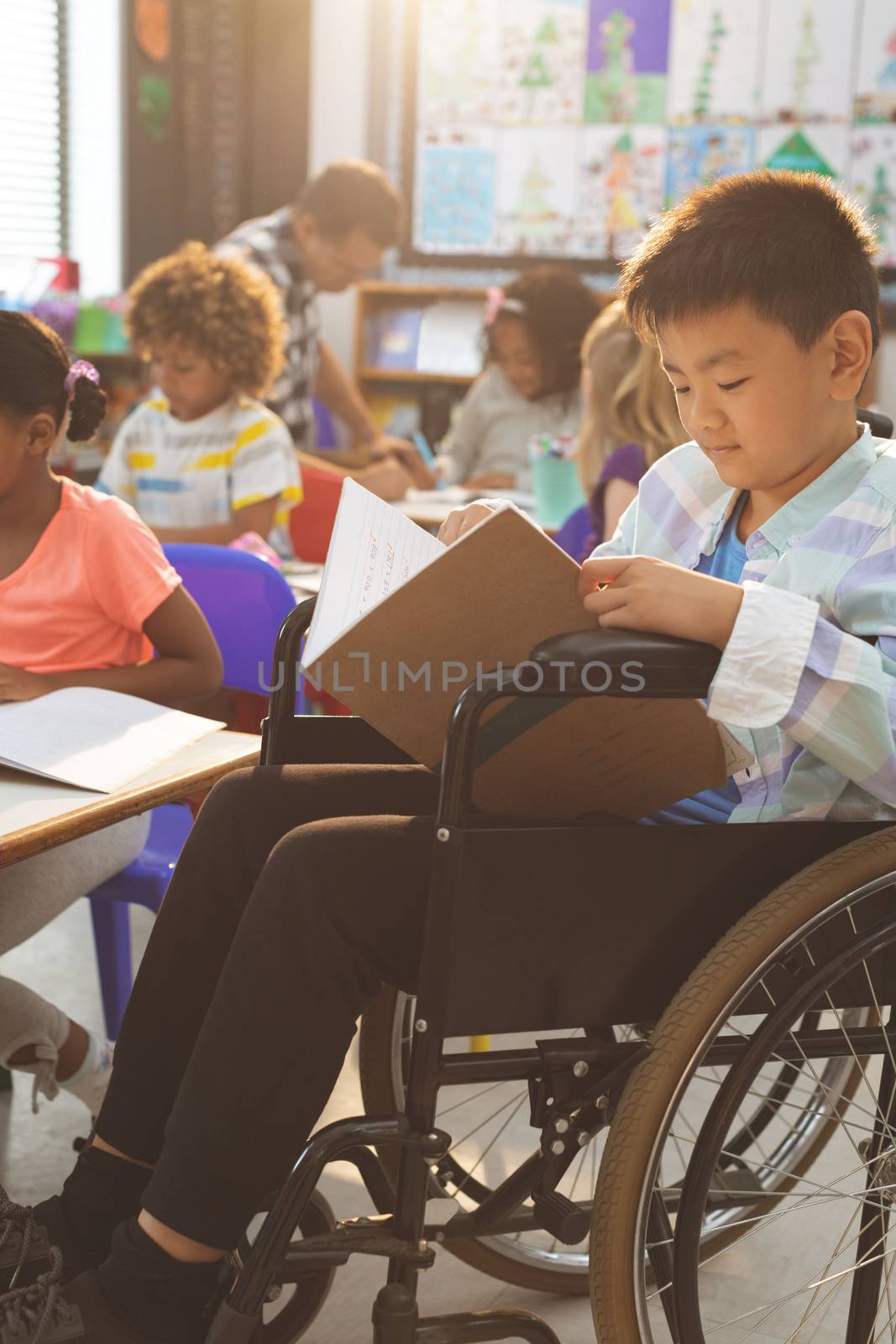 Side view of schoolboy studying in classroom while sitting at wheelchair in classroom at school