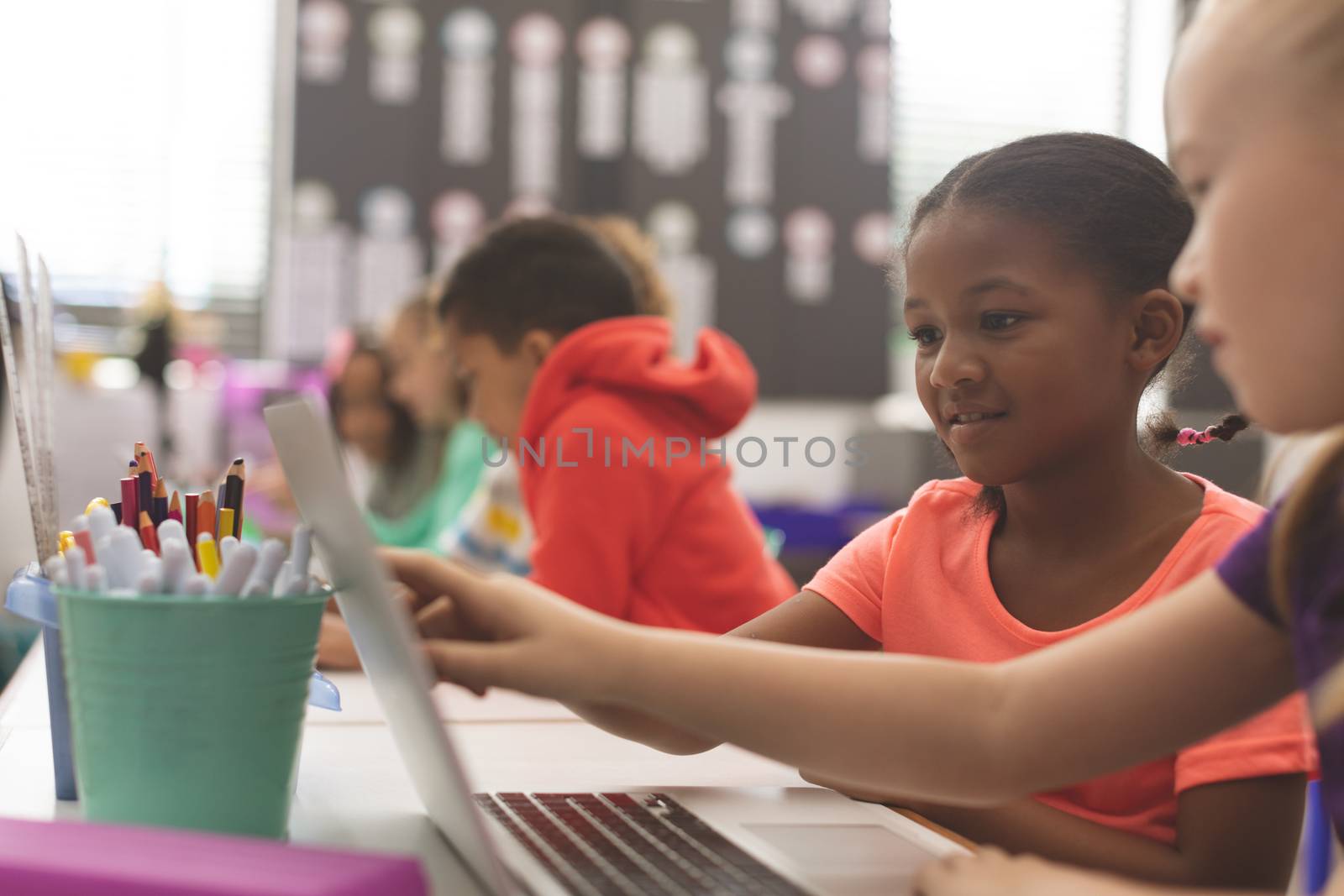 Side view of mixte ethnicity school girls using laptop in classroom at school against others school kids doing same 