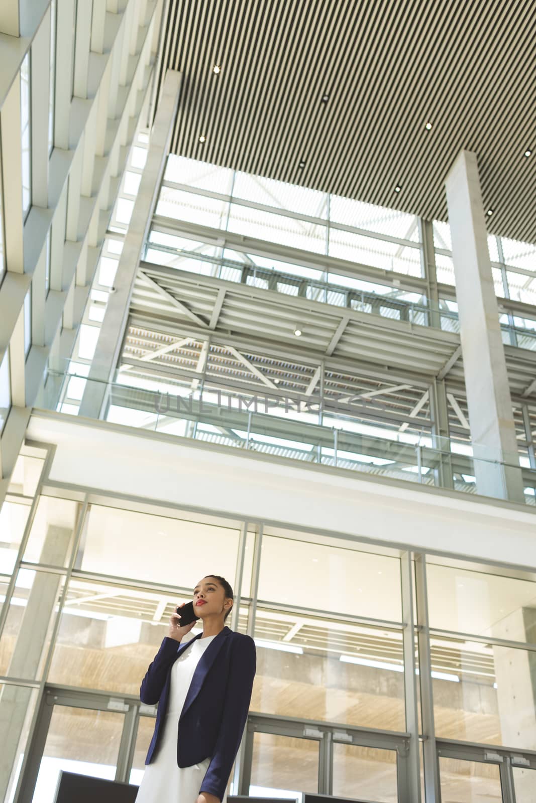 Low angle view of beautiful young mixed race businesswoman talking on mobile phone in office lobby