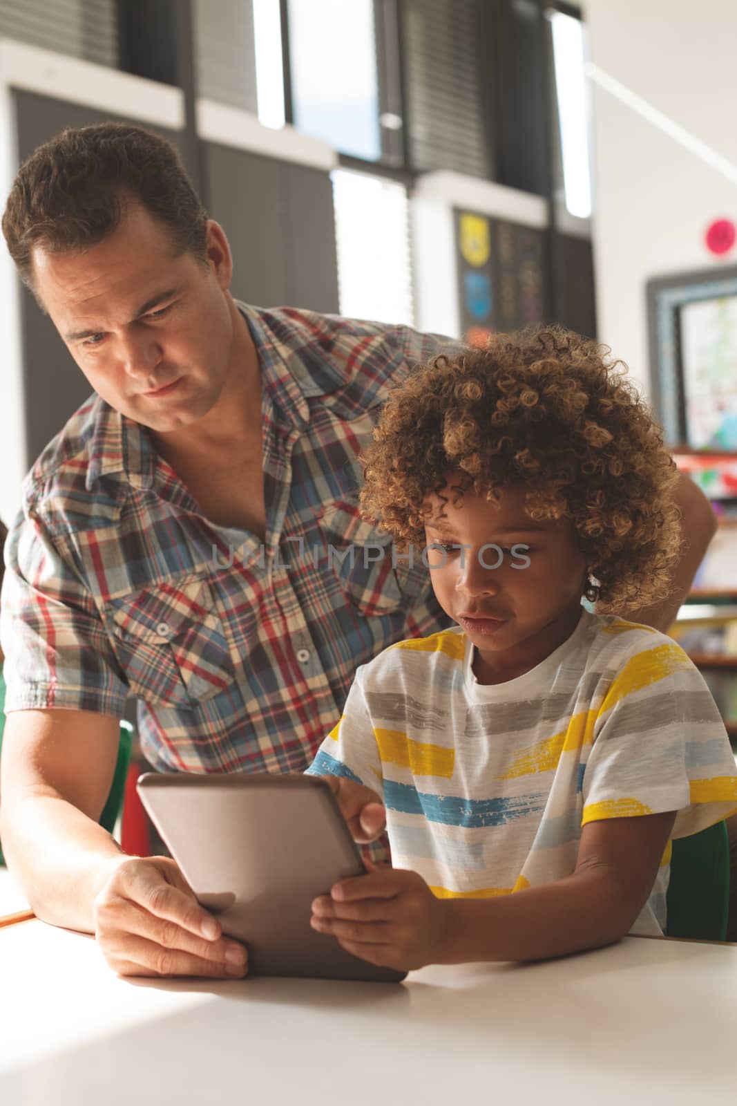 Front view of teacher and schoolboy discussing over digital tablet in classroom at school