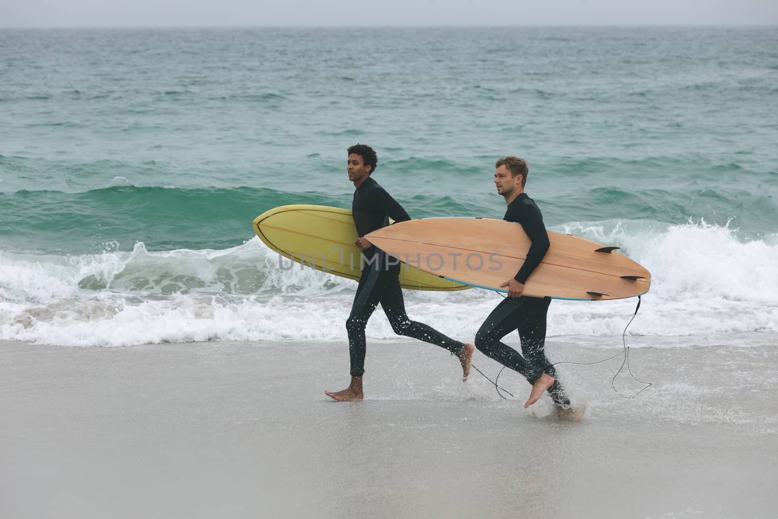 Side view of young multi-ethnic male friends running on beach while holding surfboards