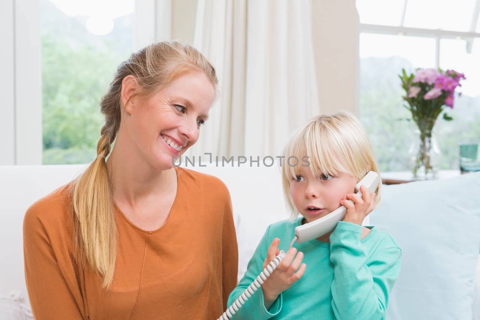 Happy mother and daughter on the couch on the phone at home in the living room