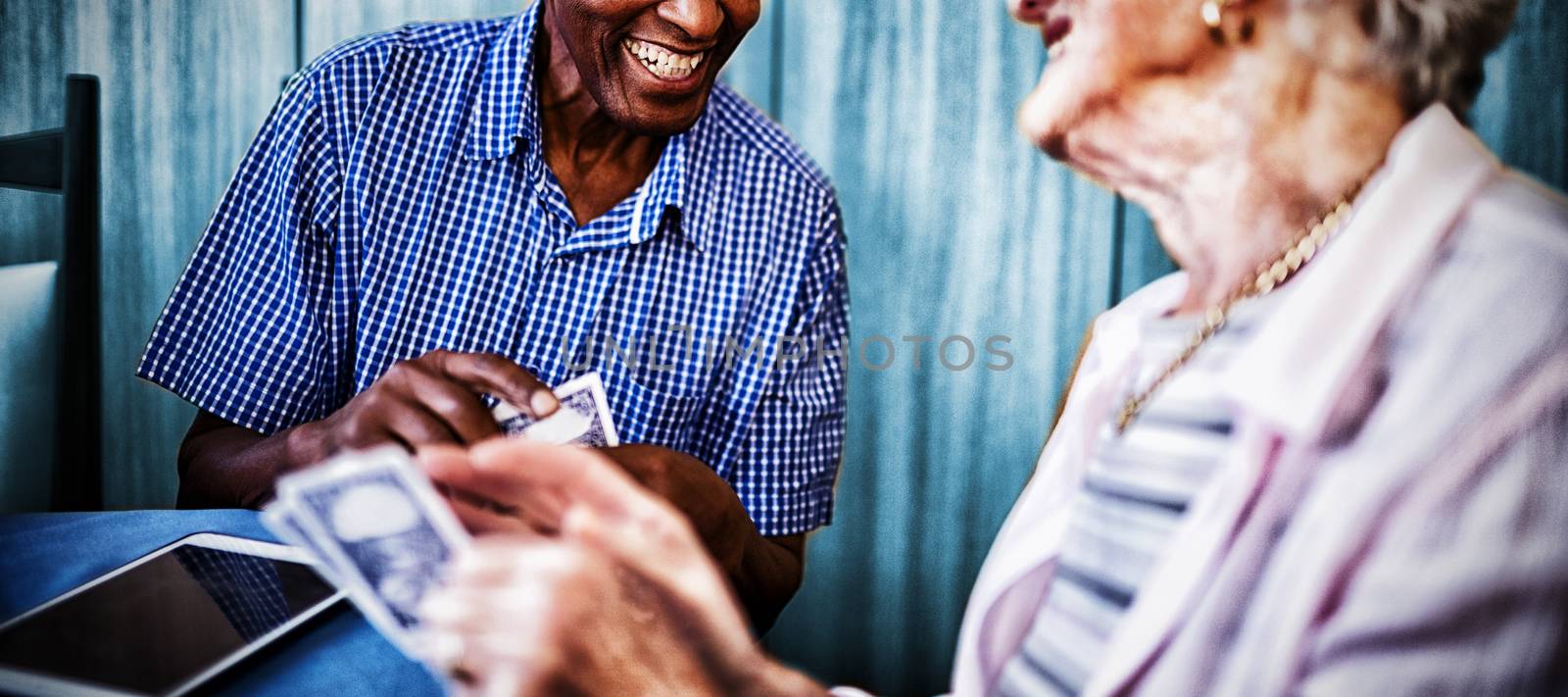 Smiling senior male and female friends playing cards at table in nursing home