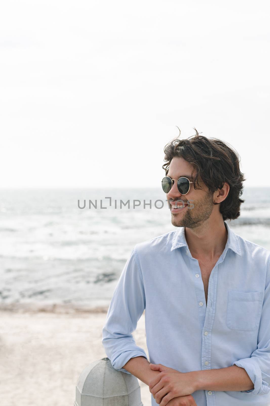 Side view of young Caucasian man standing at beach on a sunny day. He is looking away and smiling