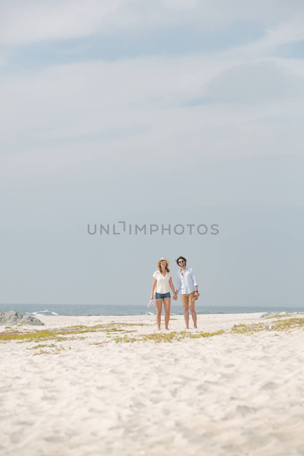 Front view of young Caucasian couple standing hand in hand at beach on a sunny day 
