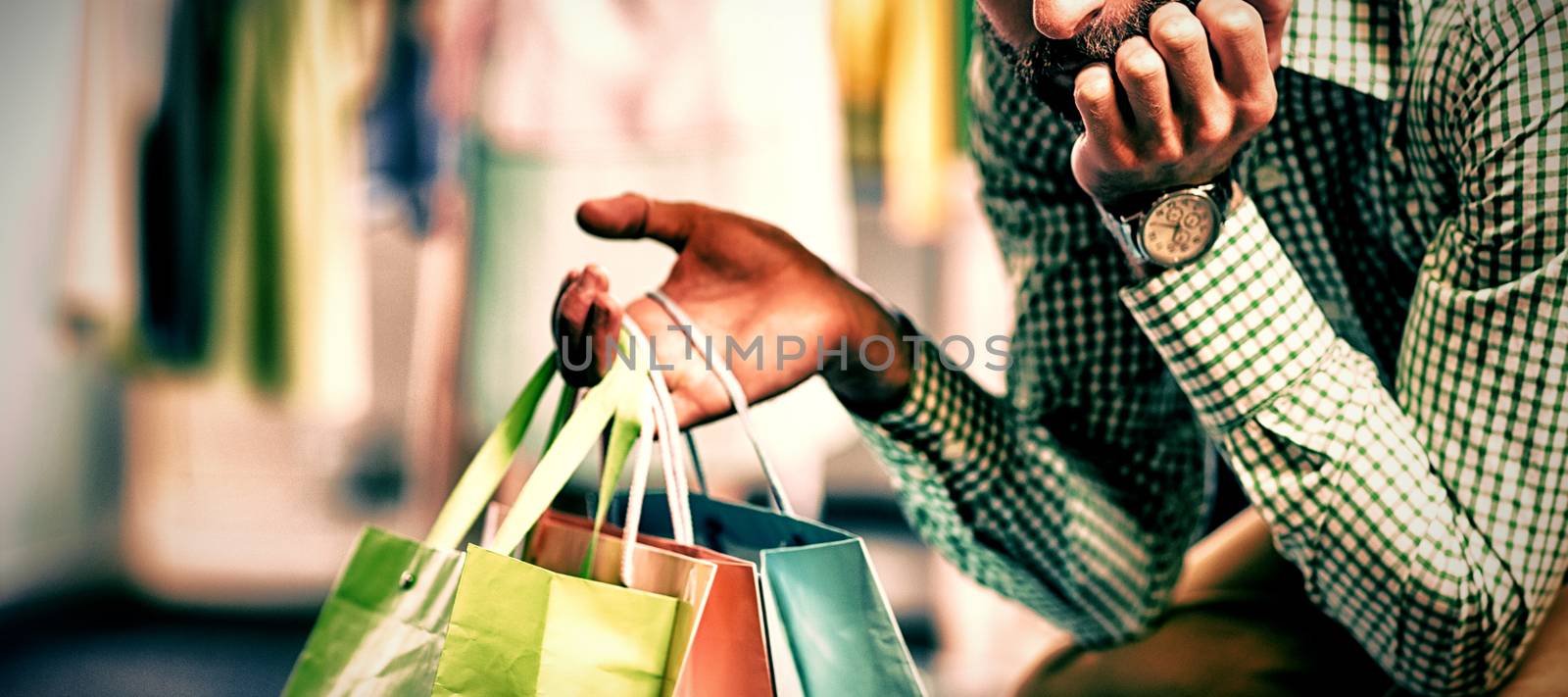 Bored man with shopping bags while woman by clothes rack in a shop