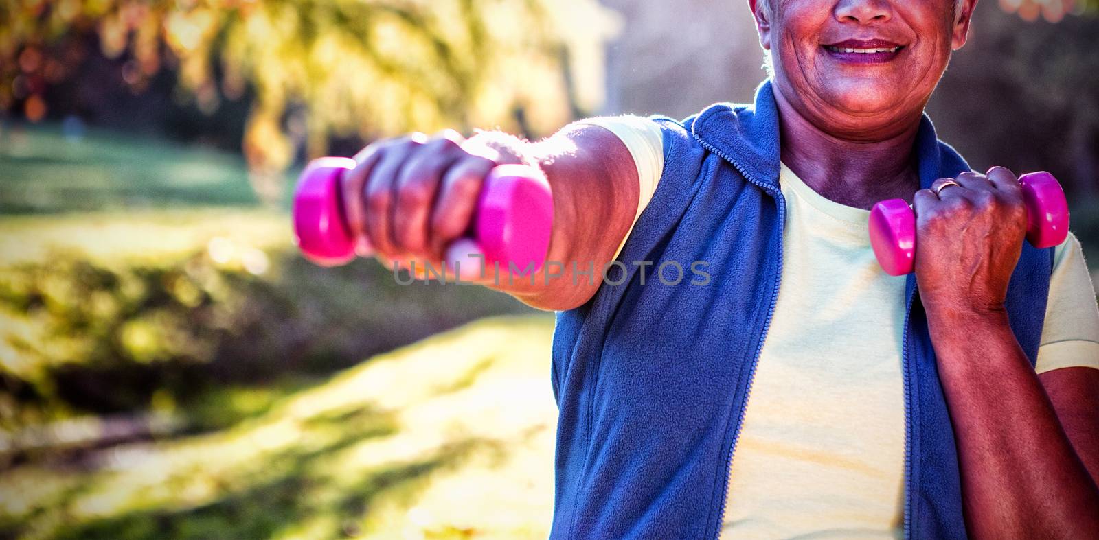 Portrait of smiling mature woman exercising with dumbbell at park