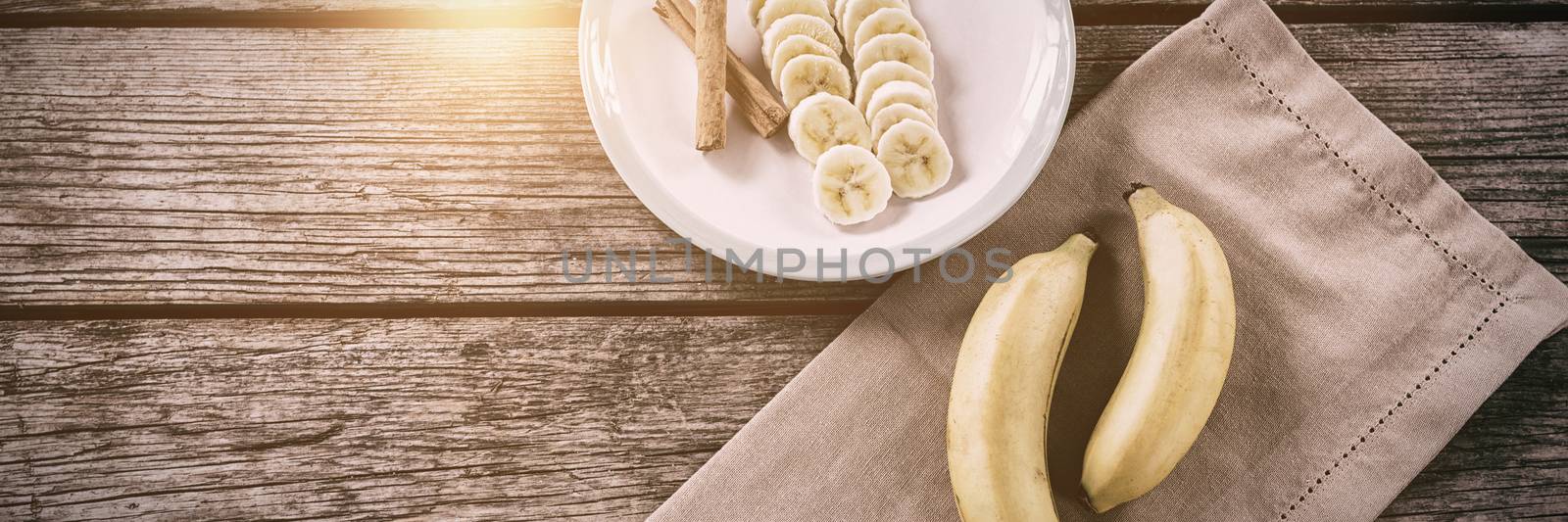 Banana and slices of banana with cinnamon stick in plate on wooden table by Wavebreakmedia