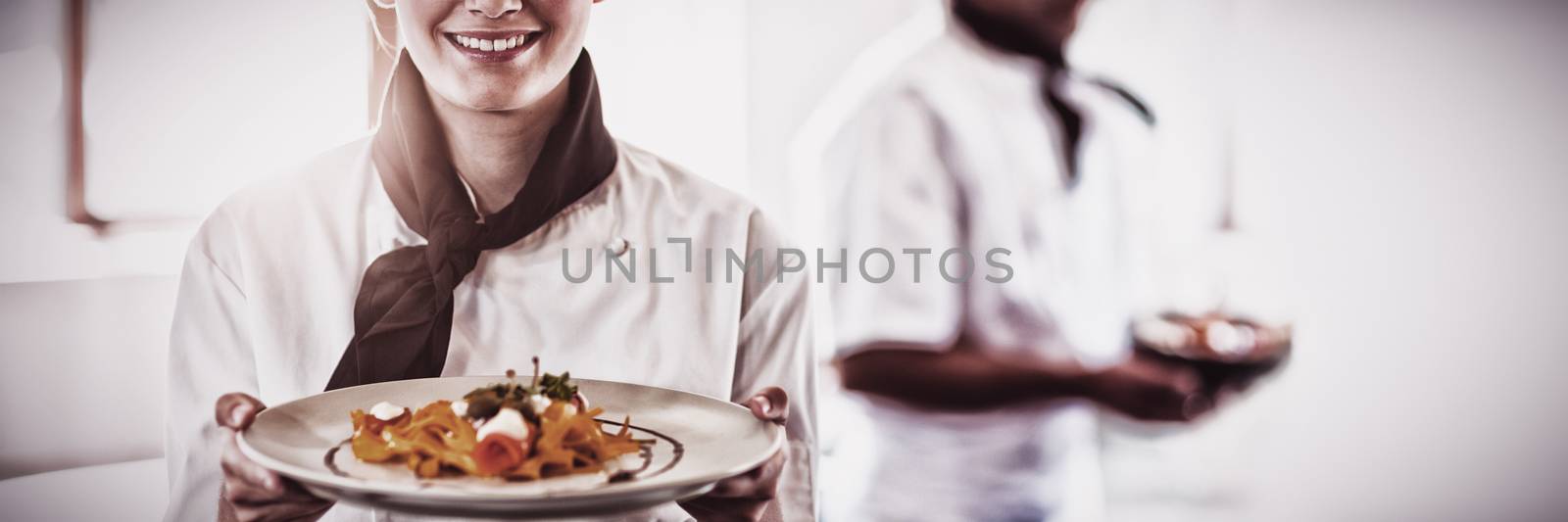 Happy head chef presenting her food in the commercial kitchen while chef working behind her