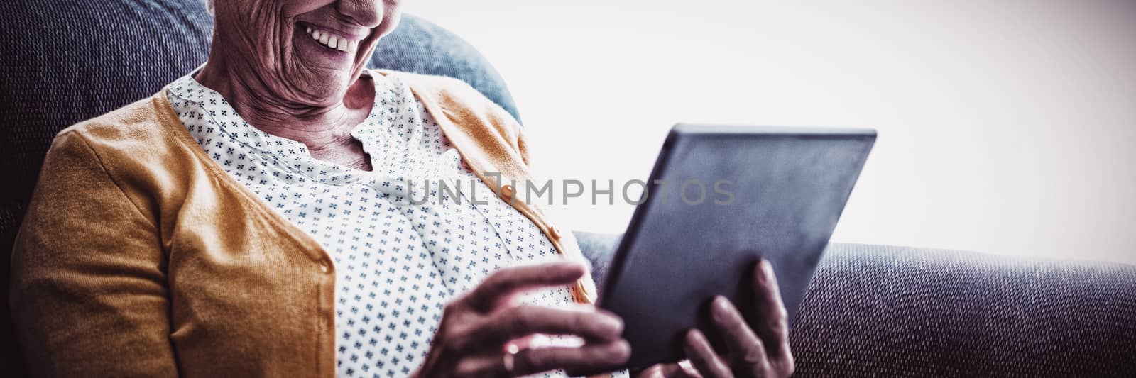 Smiling senior woman looking and laughing at her digital tablet by Wavebreakmedia