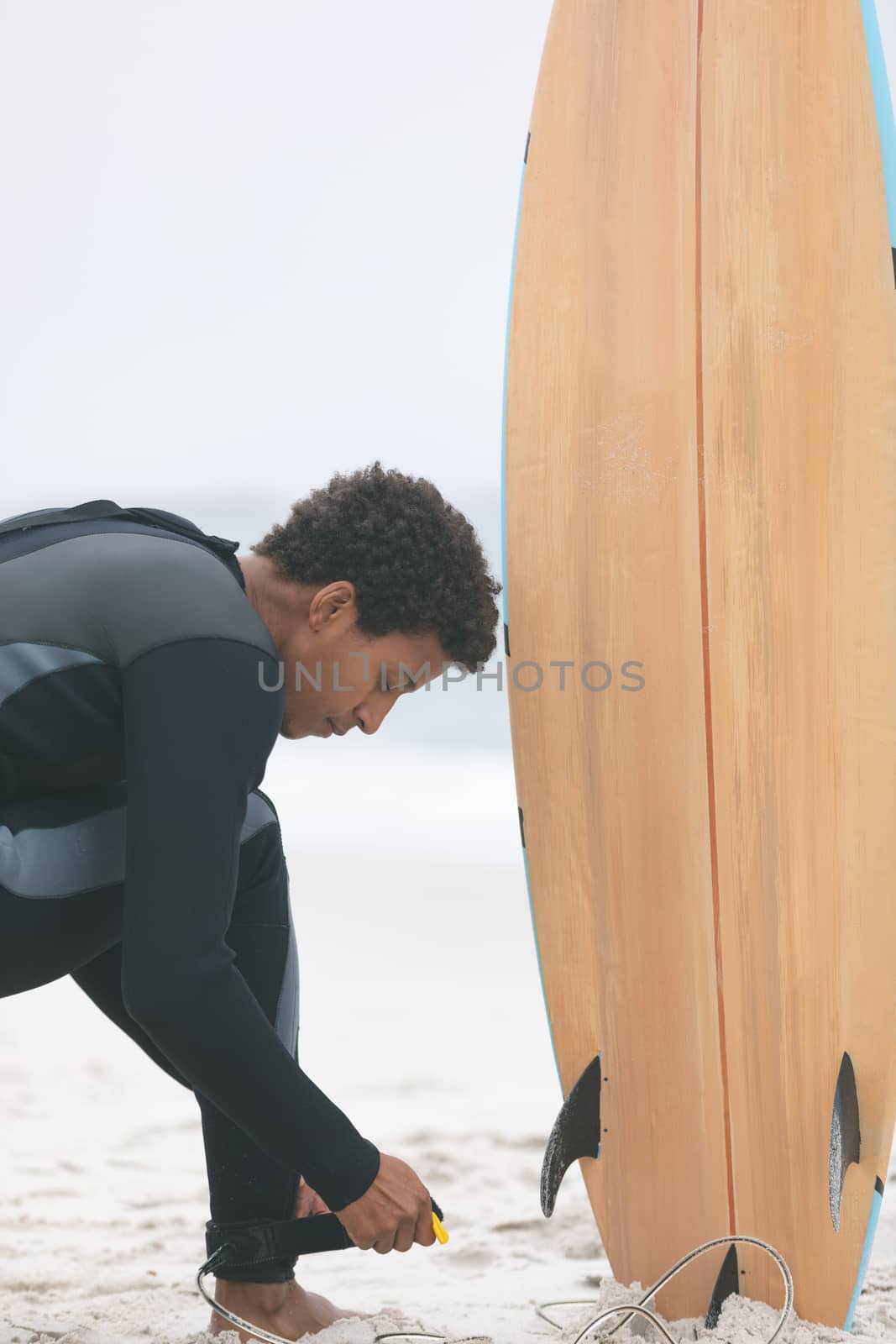 Close up of young mixed-race male surfer tying surfboard leash on his leg at beach