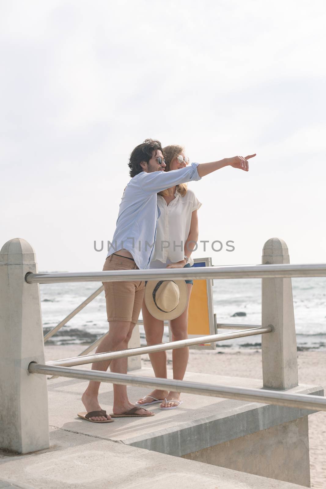 Side view of young Caucasian couple interacting with each other on the promenade at the seaside. They are looking away