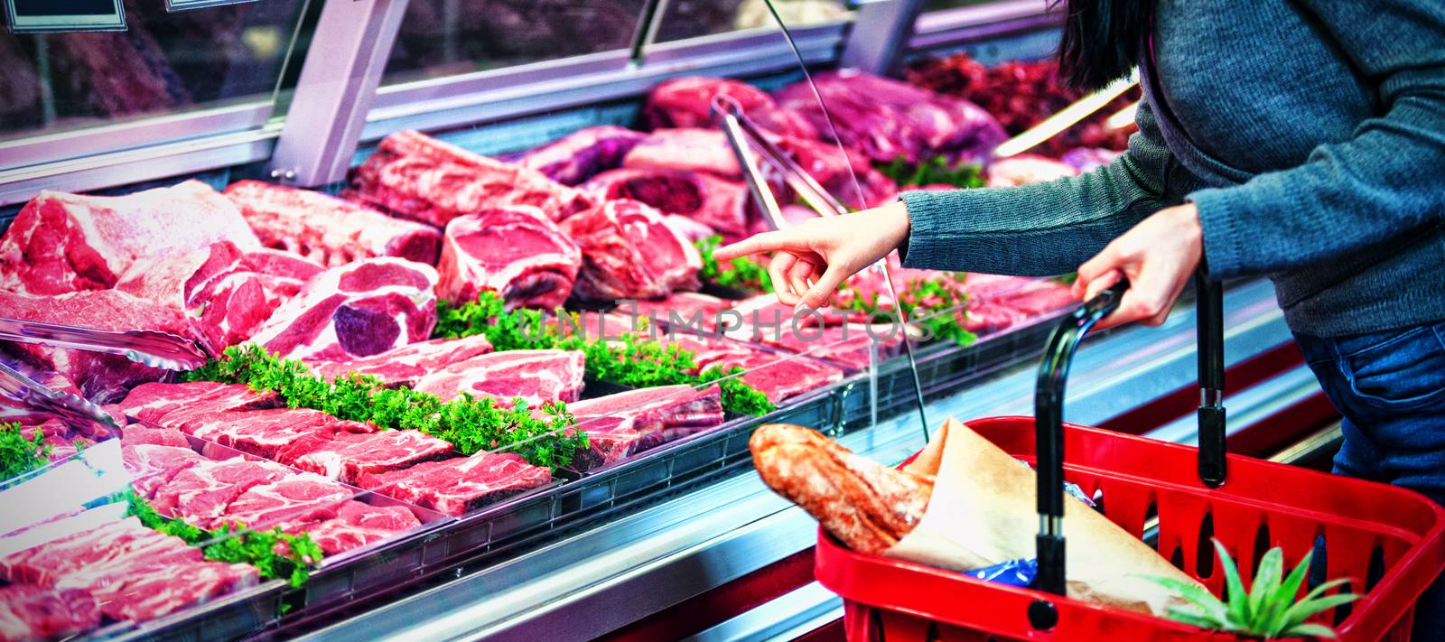 Mid section of woman pointing at meat in display at supermarket
