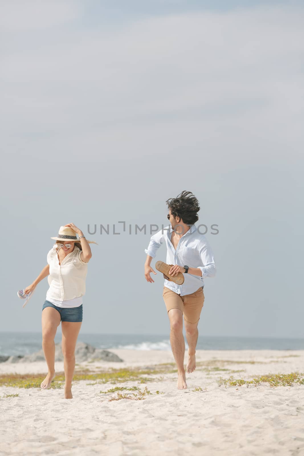 Front view of happy young Caucasian couple running at beach on sunny day. They are smiling