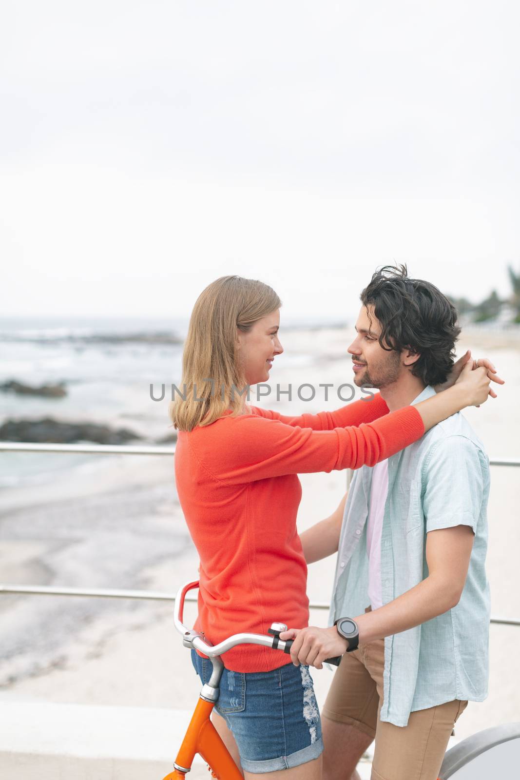 Side view of romantic younfg Caucasian couple embarrassing each other on cycle at beach. They are smiling