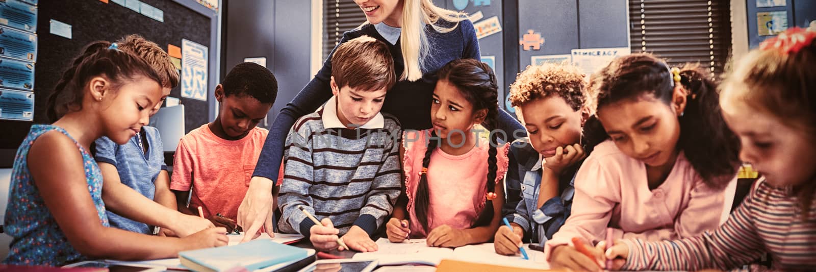 Teacher helping schoolgirl with her homework in classroom at school