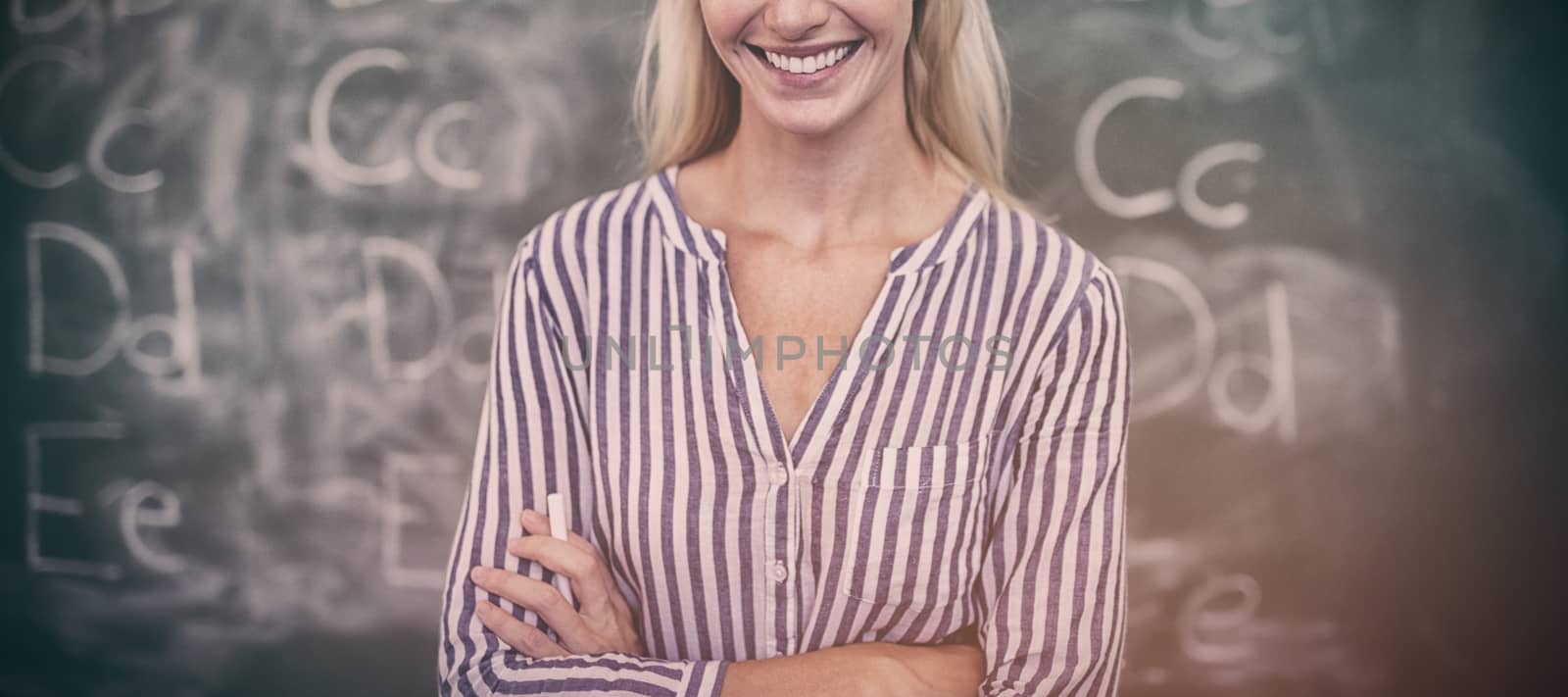 Portrait of happy teacher standing with arms crossed in classroom by Wavebreakmedia