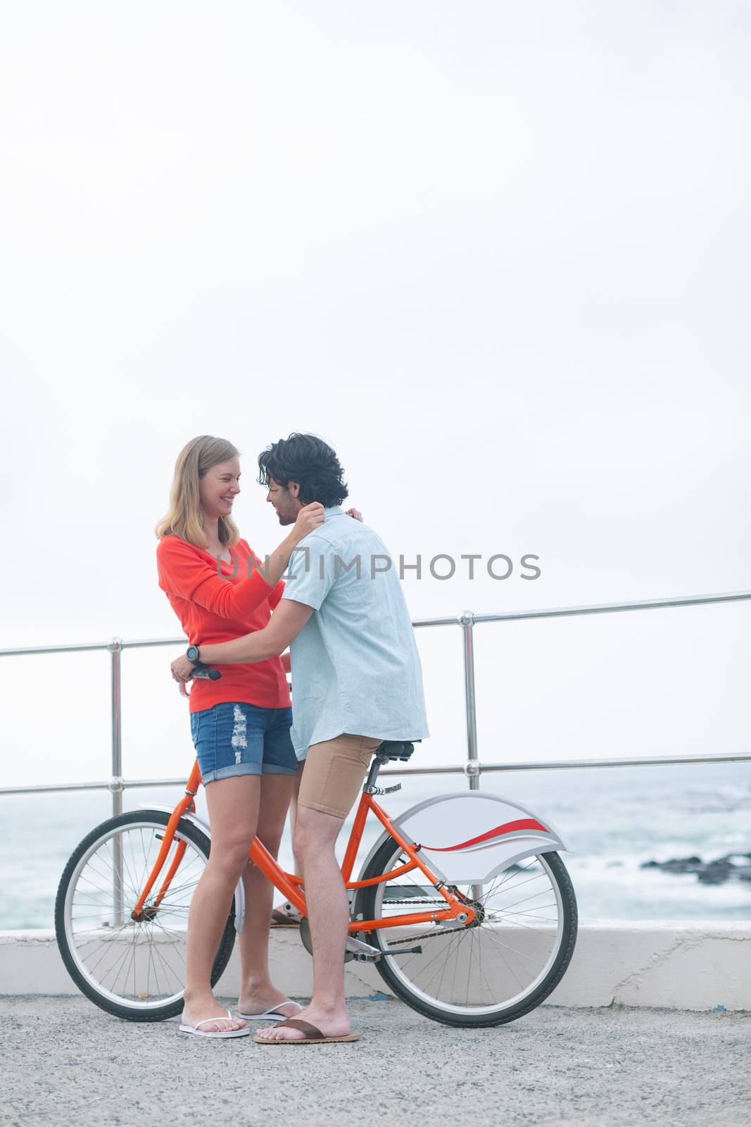 Side view of romantic young Caucasian couple embarrassing each other on cycle at beach. They are smiling 