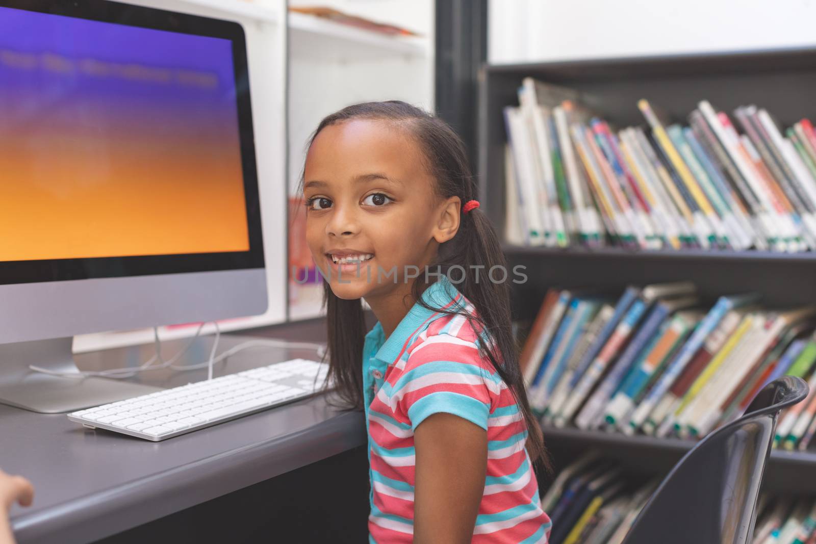 Portrait of happy African-american schoolgirl sitting and looking at camera  in computer room 