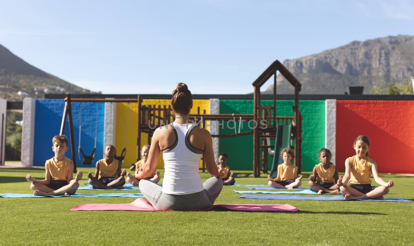 Rear view of Caucasian teacher teaching yoga lotus pose to multi ethnic students in school playground at schoolyard