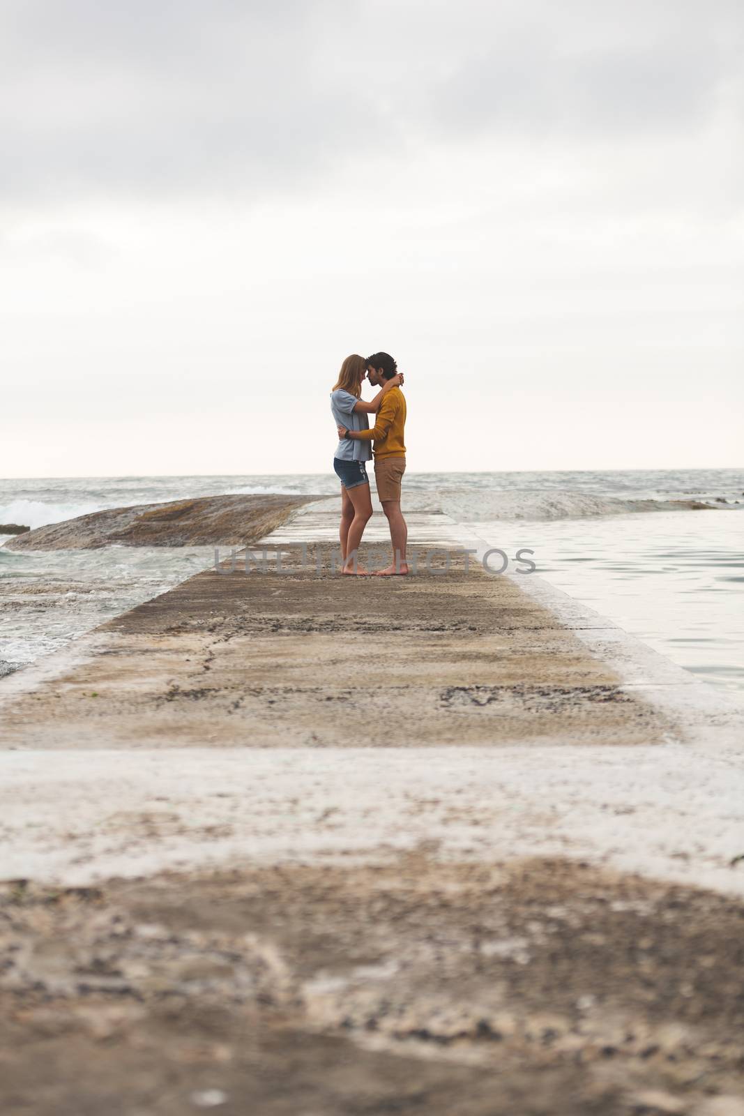 Side view of young Caucasian couple kissing each other standing on rock with arm around near beach 