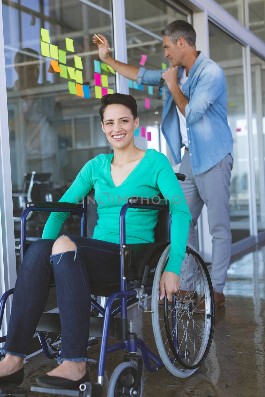 Disabled businesswoman looking at camera while male executive writing on sticky notes in office