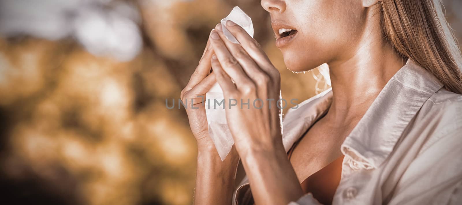 Beautiful woman using tissue while sneezing in park