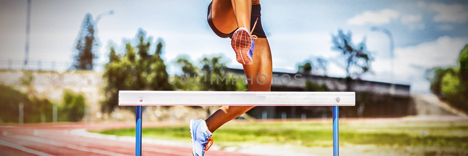Female athlete jumping above the hurdle by Wavebreakmedia