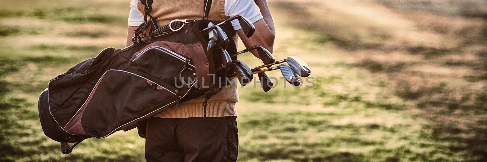 Man carrying golf bag while standing on field by Wavebreakmedia