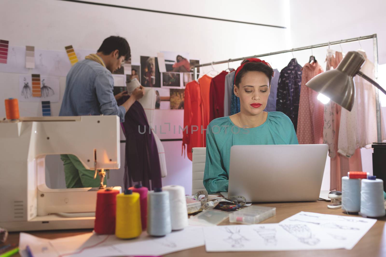 Female fashion designer working on laptop while male fashion designer dressing mannequin by Wavebreakmedia