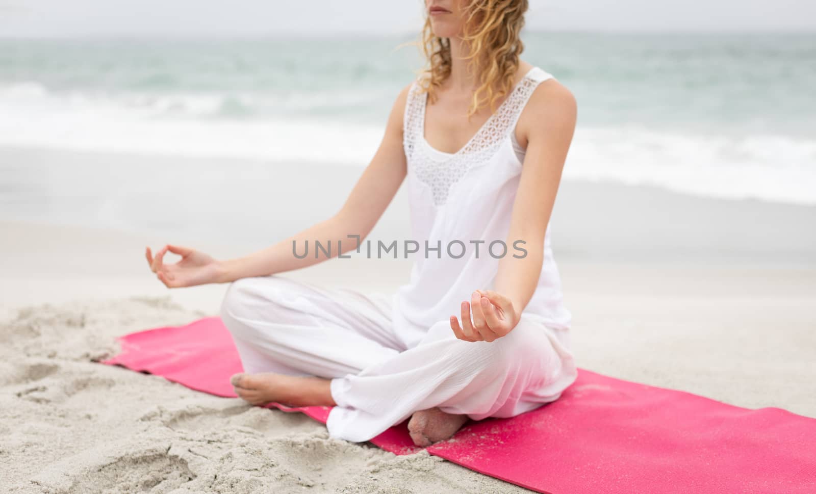 Front view of beautiful caucasian woman performing yoga on lotus pose at beach on sunny day