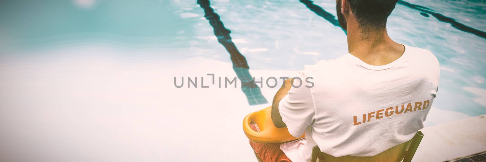 Lifeguard sitting on chair with rescue buoy at poolside by Wavebreakmedia