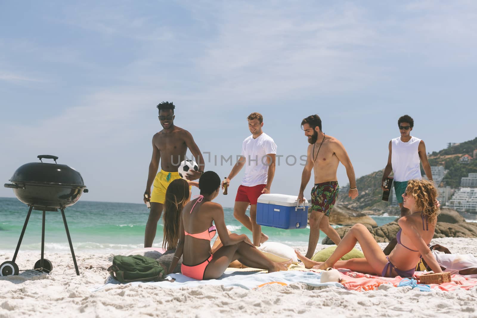 Front view of multi ethnic group of friends relaxing and enjoying at beach on a sunny day. Preparing barbecue