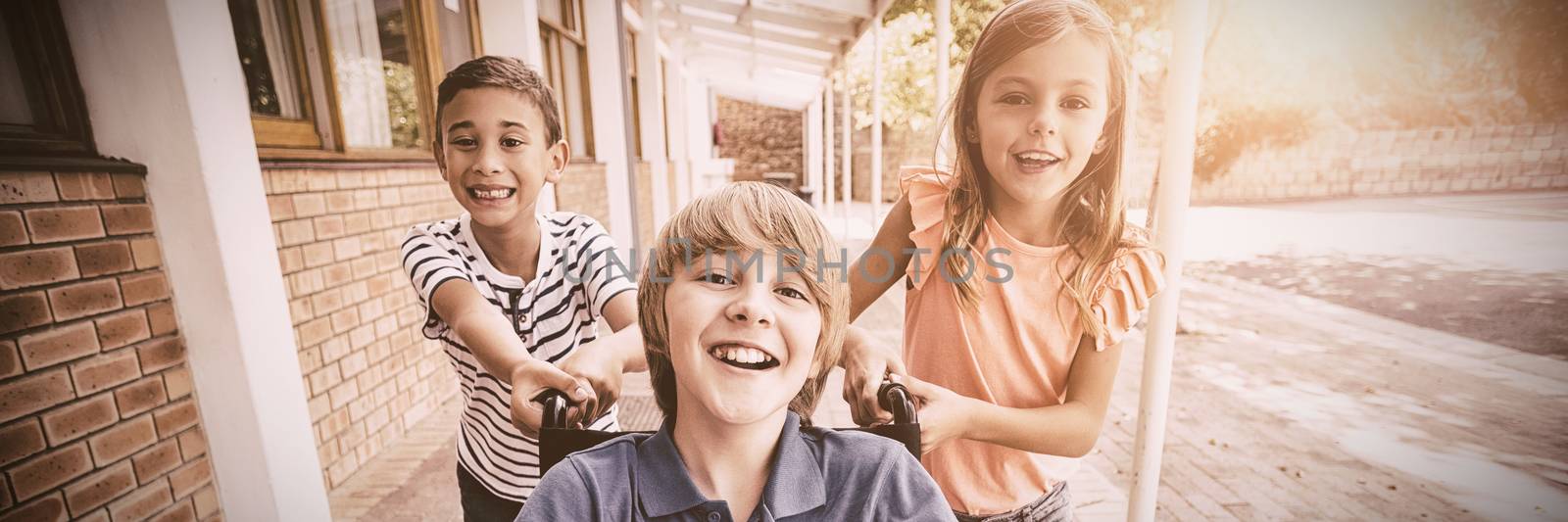 Portrait of school kids pushing a boy on wheelchair in school corridor