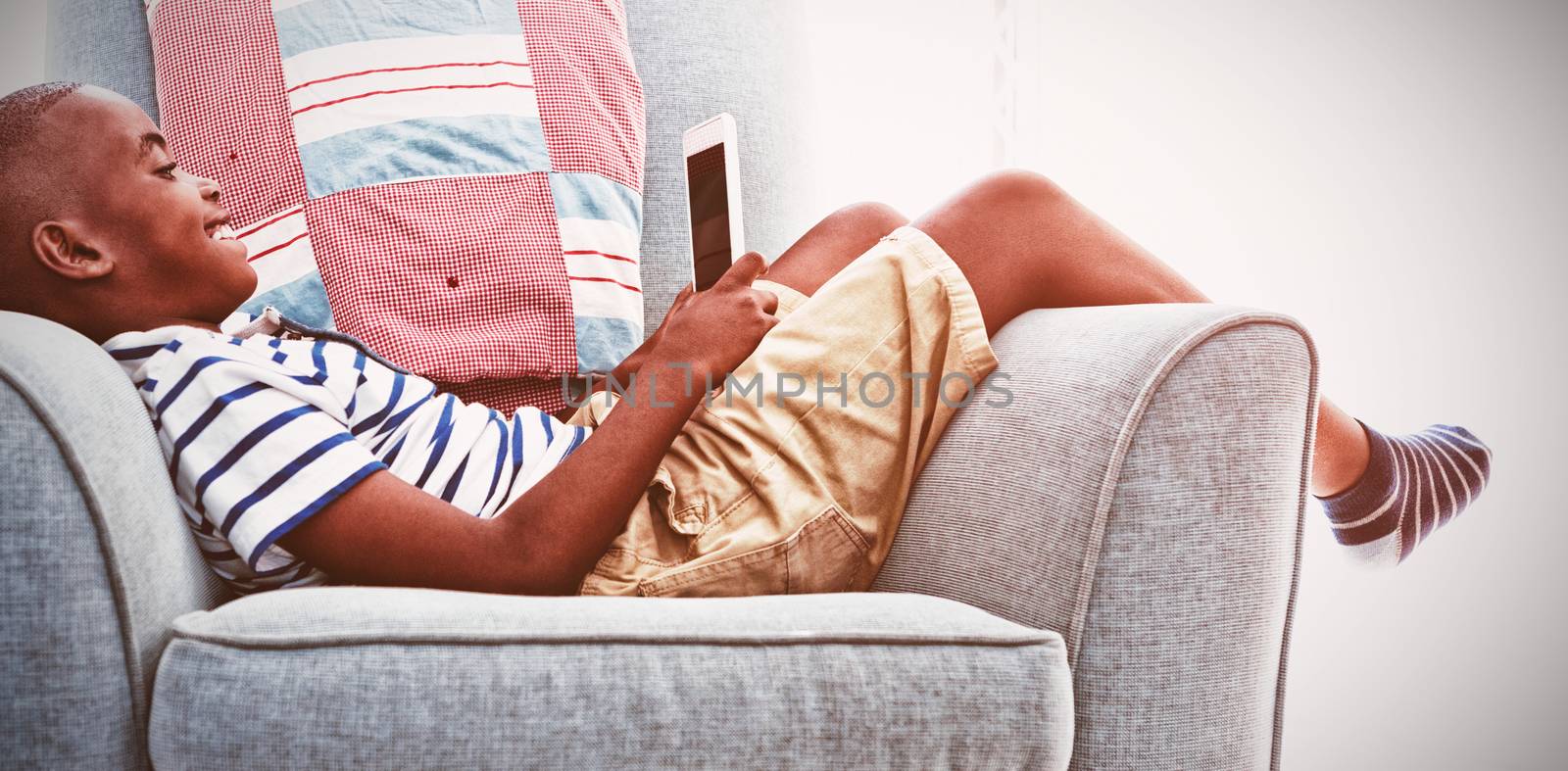 Side view of smiling boy looking at mobile phone while lying on armchair by Wavebreakmedia